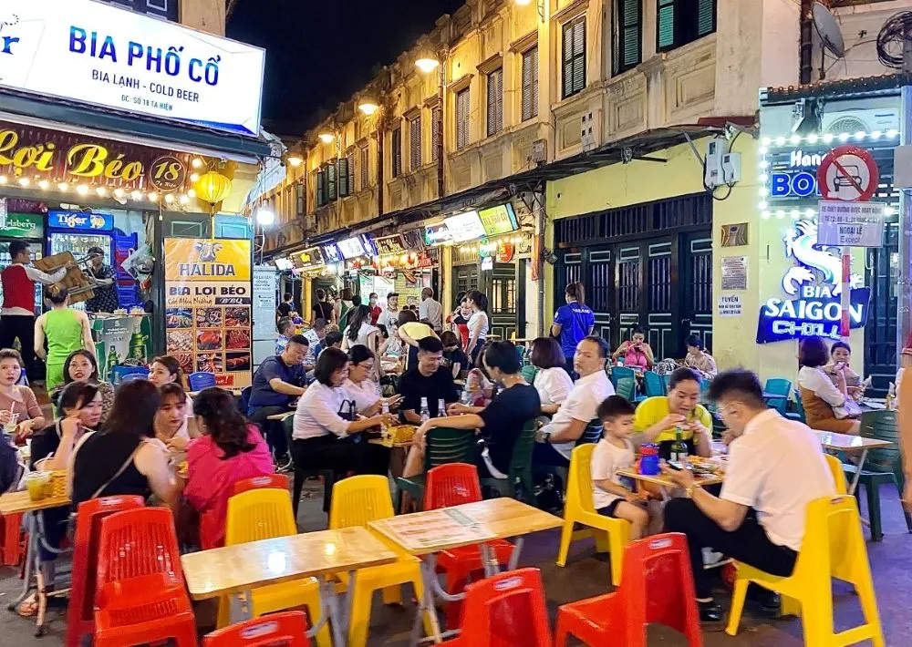 Turisti e residenti bevono Bia Hoi fresca su sgabelli di plastica a Beer Street Hanoi