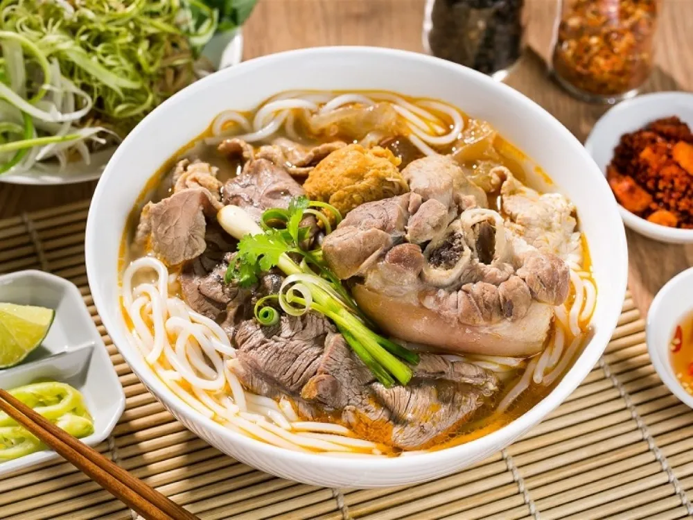 Spicy bun bo hue with thick noodles, beef, pork knuckle, and a bright red lemongrass broth