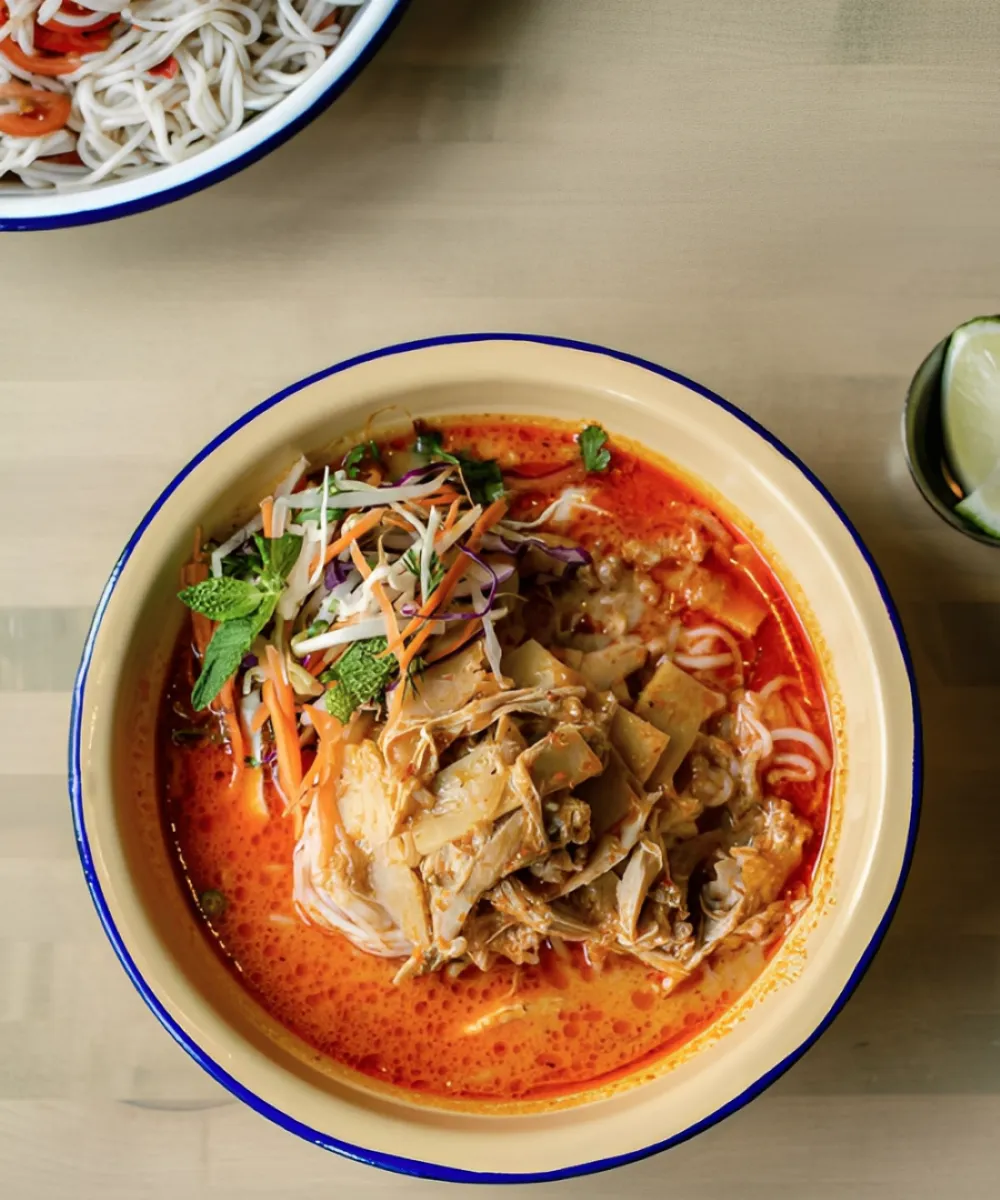 Khao Poun a fragrant spicy vermicelli soup with creamy coconut milk curry broth and fresh herbs on top