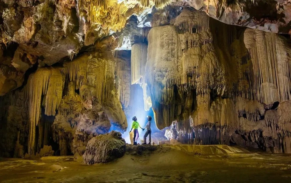 Adventurous travelers trekking through a massive, dramatic cave system in Phong Nha-Ke Bang