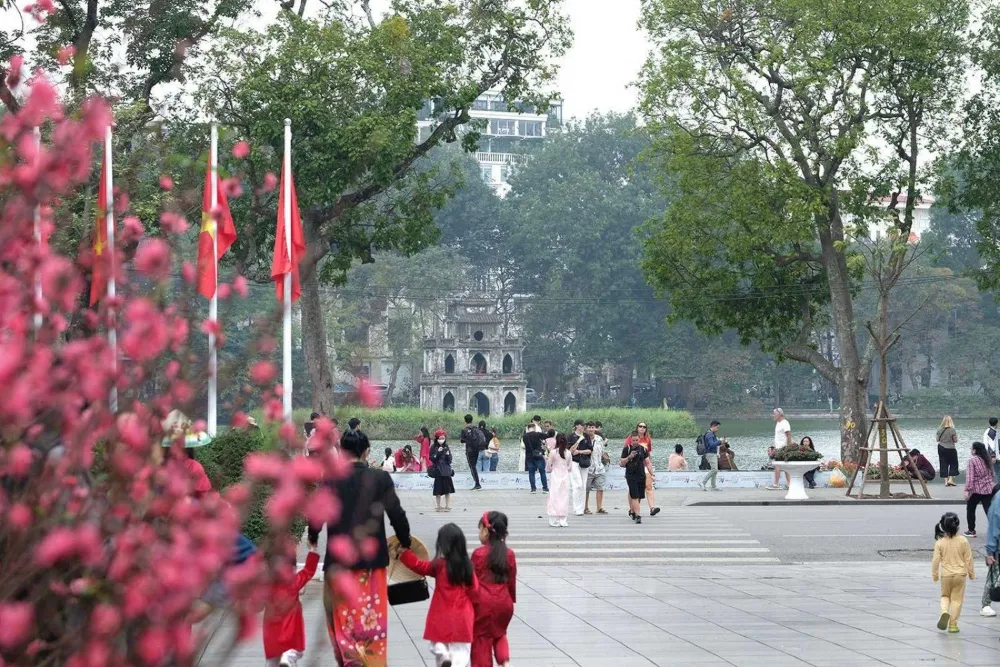 Families and tourists walking near Hoan Kiem Lake and Turtle Tower in Hanoi