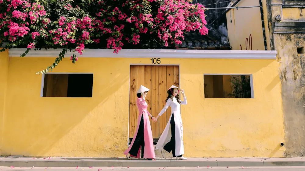 Turista posando en un Ao Dai vibrante junto a una pared amarilla en Hoi An