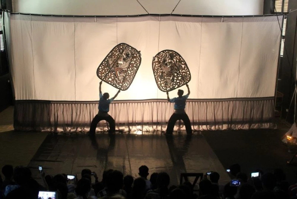 Puppeteers holding giant bamboo poles to manipulate large leather silhouettes behind a illuminated screen at a night performance in Siem Reap